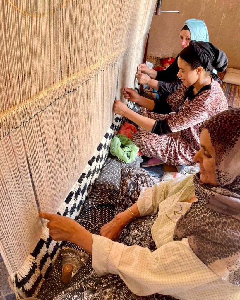 The ladies in front of the weaver are working on the art of carpeting by hand 820x1024 Moroccan Rug Weaving Process.